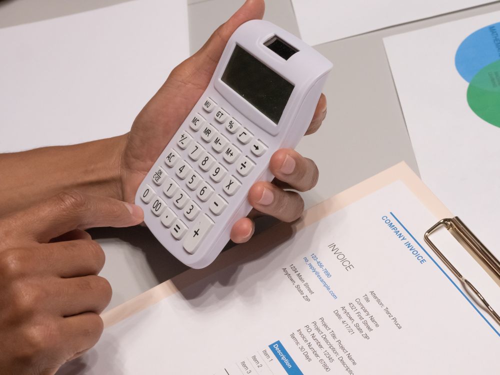 A hand holding a calculator over an invoice